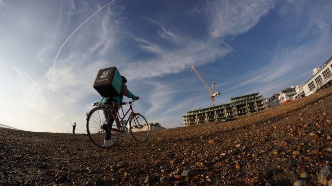 A Deliveroo driver treks into a construction site. Those working for Deliveroo and other gig economy companies like Uber and Amazon should be classified as workers, says a report by the Work and Pensions Committee.